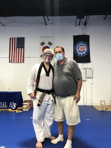 Alex Kagen and his father smile at the camera. Kagen is dressed in a martial arts gi. The photo was taken in a martial arts studio.