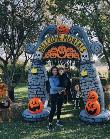 Grace Lozinski holds her daughter on her hip. They are standing under an inflatable decorative Halloween arch outside.
