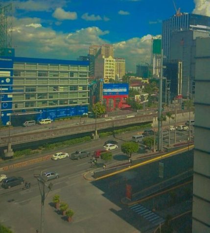 A picture taken on a phone of Manila, the capital of the Philippines. The picture seems to have been taken from a tall building's window, as it shows the city street below and the skyline up close.