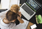 stock photo of woman holding head with homework and a laptop in front of her